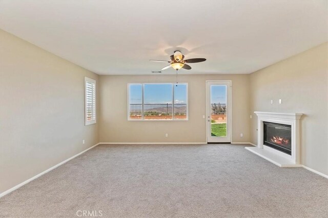 unfurnished living room featuring visible vents, baseboards, a glass covered fireplace, ceiling fan, and carpet