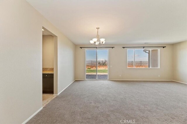 spare room featuring light carpet, a notable chandelier, and baseboards