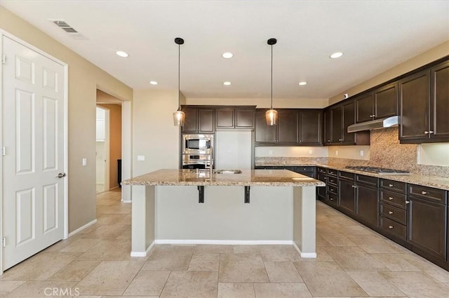 kitchen with visible vents, appliances with stainless steel finishes, a kitchen island with sink, dark brown cabinets, and under cabinet range hood