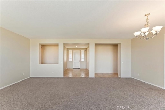 spare room featuring a chandelier, light colored carpet, and baseboards