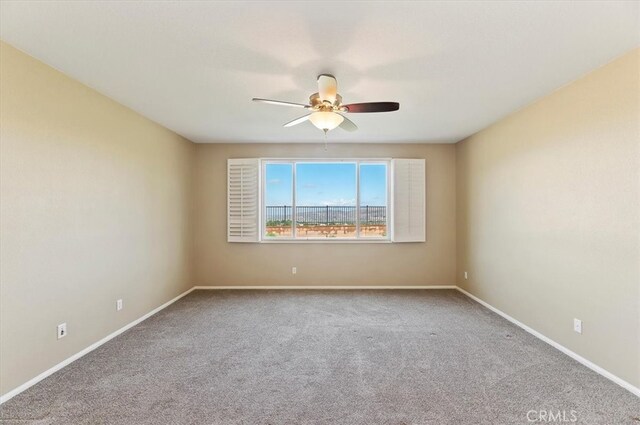 carpeted spare room with a ceiling fan and baseboards