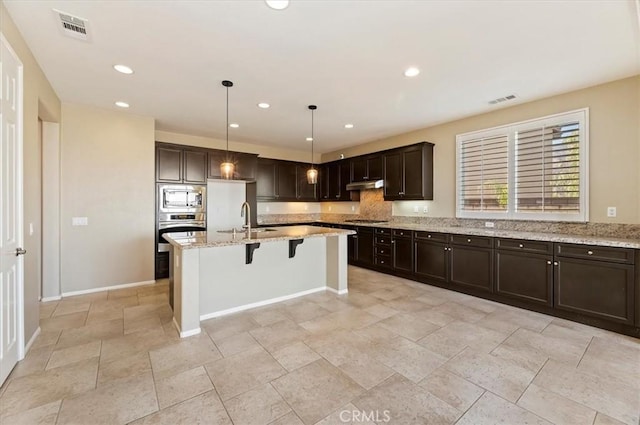 kitchen with light stone countertops, under cabinet range hood, visible vents, and appliances with stainless steel finishes