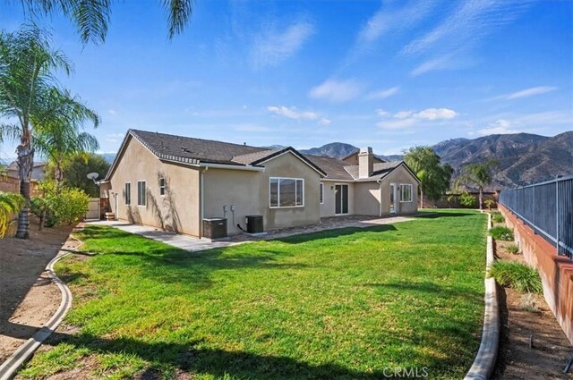 back of house with a lawn, a fenced backyard, a mountain view, and stucco siding