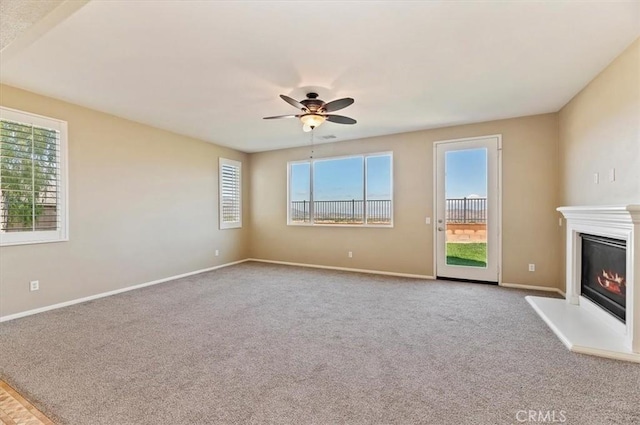 unfurnished living room featuring carpet floors, ceiling fan, baseboards, and a glass covered fireplace