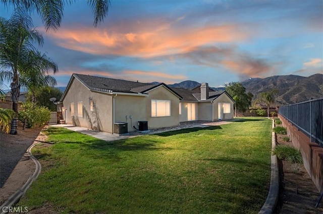 back of property at dusk with a yard, a fenced backyard, a mountain view, and stucco siding