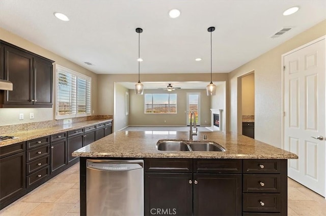 kitchen featuring a warm lit fireplace, stainless steel appliances, a sink, visible vents, and an island with sink