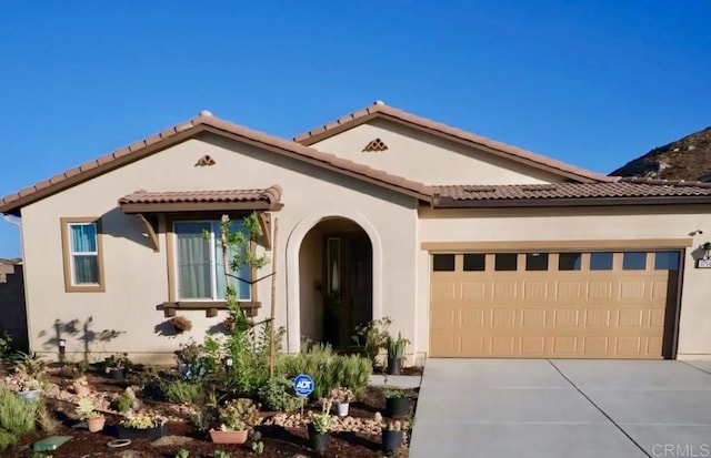 mediterranean / spanish house with driveway, an attached garage, a tile roof, and stucco siding