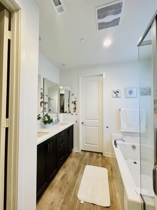 bathroom featuring double vanity, visible vents, a sink, wood finished floors, and a bath