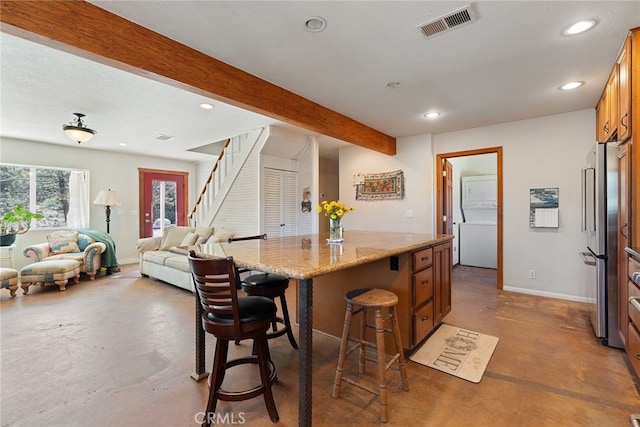 kitchen featuring visible vents, beamed ceiling, finished concrete floors, freestanding refrigerator, and stacked washer / drying machine