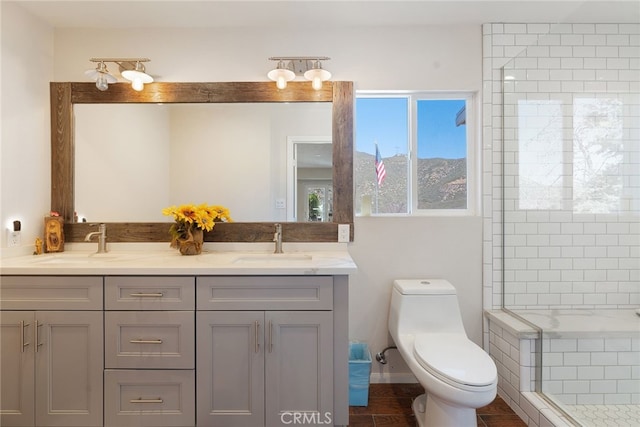 full bath featuring double vanity, a tile shower, toilet, and a sink