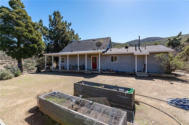 rear view of house featuring stucco siding, a vegetable garden, and a mountain view