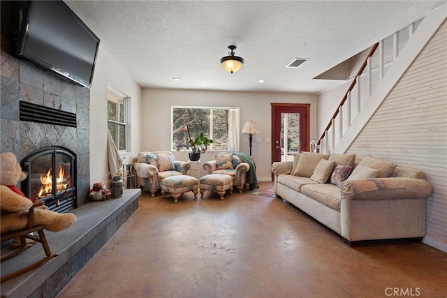 living room featuring visible vents, a textured ceiling, finished concrete floors, a glass covered fireplace, and stairway