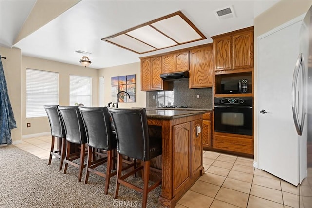 kitchen with visible vents, under cabinet range hood, black appliances, and light tile patterned floors