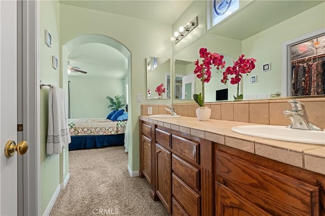 ensuite bathroom featuring double vanity, connected bathroom, baseboards, and a sink