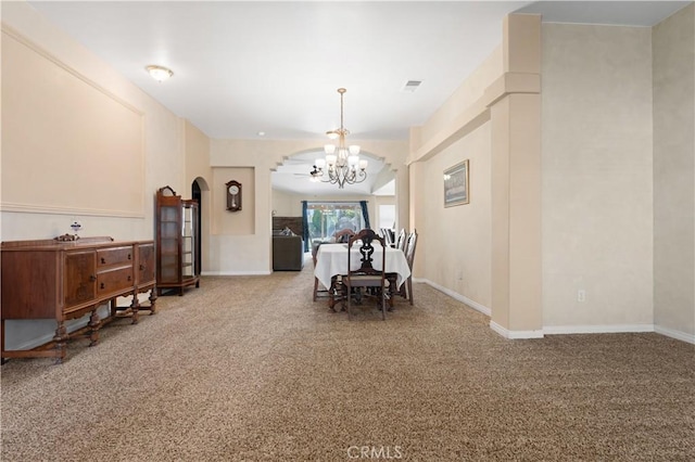 carpeted dining room featuring baseboards, visible vents, arched walkways, and a chandelier