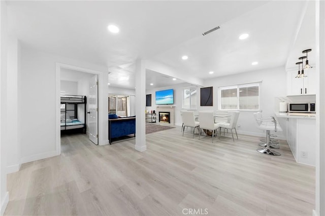 unfurnished living room with recessed lighting, visible vents, baseboards, light wood-style floors, and a glass covered fireplace