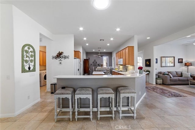 kitchen with ceiling fan, a breakfast bar, a peninsula, white appliances, and washer / clothes dryer