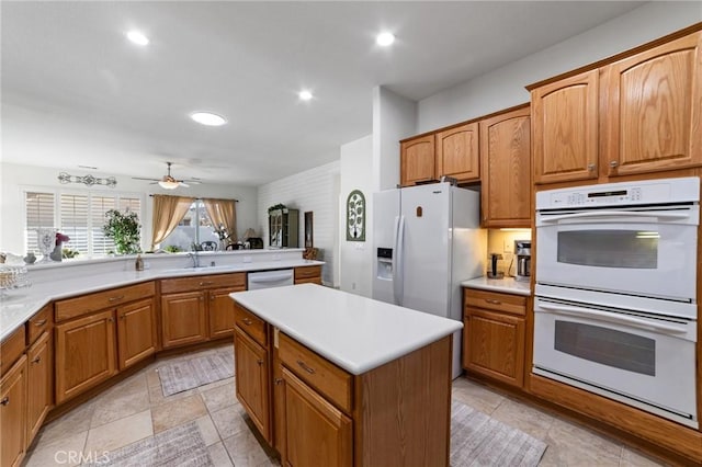 kitchen featuring white appliances, a kitchen island, ceiling fan, a sink, and light countertops