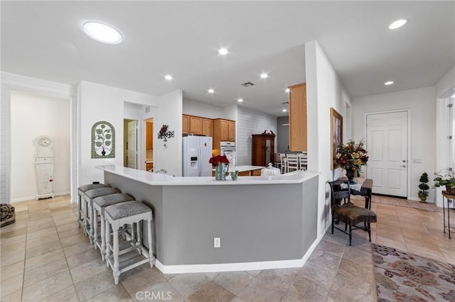 kitchen with a breakfast bar, recessed lighting, white refrigerator with ice dispenser, and light countertops