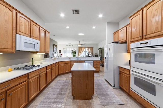 kitchen featuring visible vents, a kitchen island, light countertops, a peninsula, and white appliances