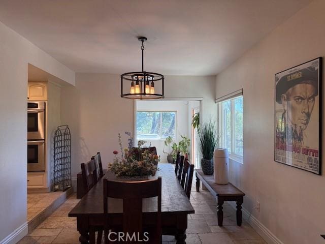 dining room featuring baseboards, stone tile floors, and an inviting chandelier