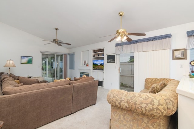 living area with ceiling fan, built in features, light colored carpet, lofted ceiling, and a glass covered fireplace