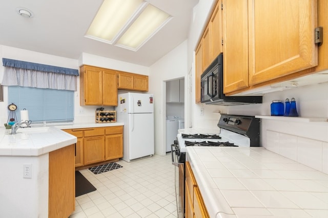 kitchen featuring tile countertops, lofted ceiling, freestanding refrigerator, black microwave, and range with gas cooktop