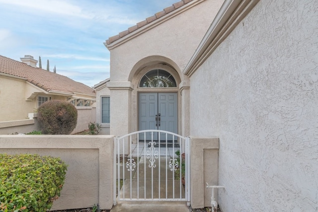 entrance to property with a gate, stucco siding, a tile roof, and fence