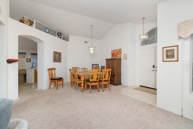 dining area with high vaulted ceiling, arched walkways, a chandelier, and light carpet