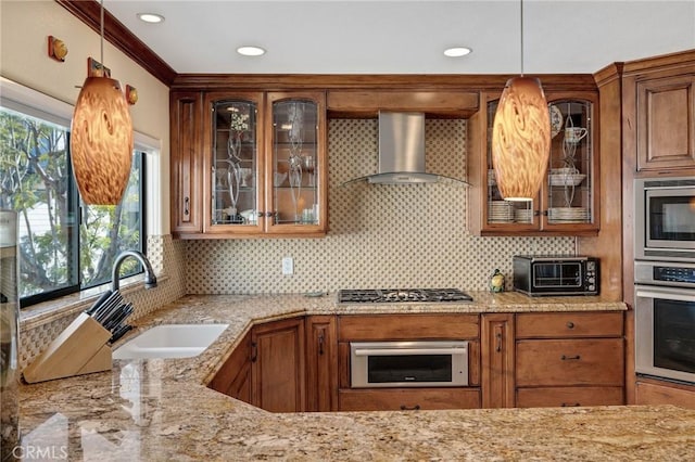 kitchen with light stone counters, a toaster, a sink, stainless steel appliances, and wall chimney exhaust hood