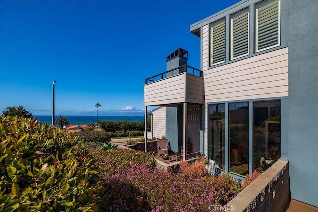 exterior space with stucco siding, a balcony, and a water view