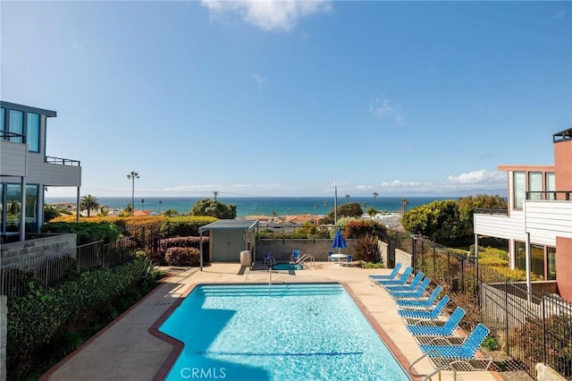 community pool featuring a patio area, a water view, and fence