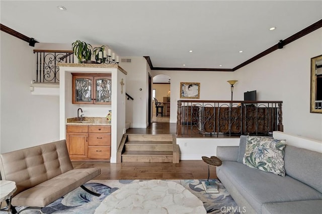 living area featuring arched walkways, visible vents, crown molding, and wood finished floors