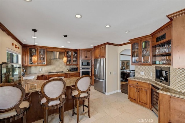 kitchen featuring light stone counters, a peninsula, a sink, stainless steel appliances, and crown molding