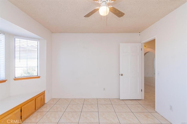 unfurnished room with a textured ceiling, arched walkways, ceiling fan, and light tile patterned floors