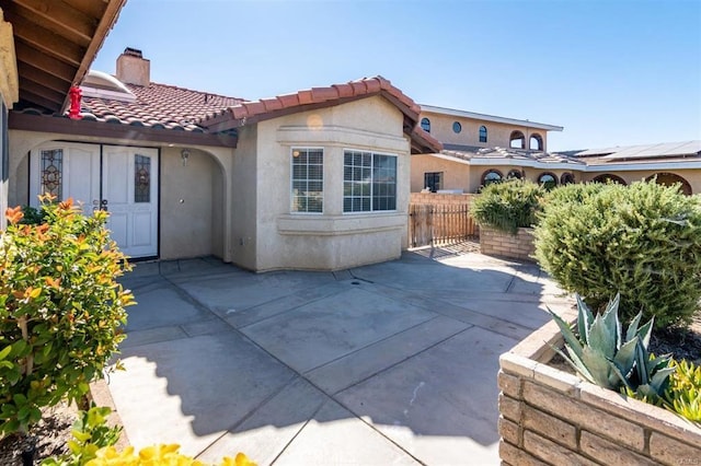 back of property featuring fence, a tiled roof, stucco siding, a chimney, and a patio area