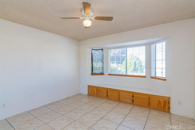 empty room featuring light tile patterned floors, a textured ceiling, and a ceiling fan