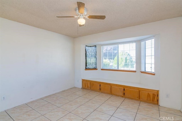 spare room featuring a ceiling fan, light tile patterned floors, and a textured ceiling