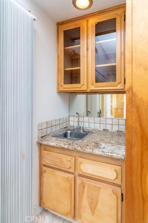 kitchen featuring glass insert cabinets, light stone countertops, and a sink