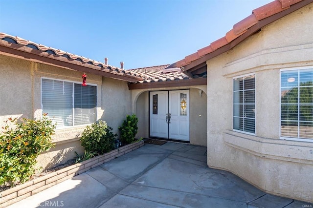 view of exterior entry with a patio area, stucco siding, and a tiled roof