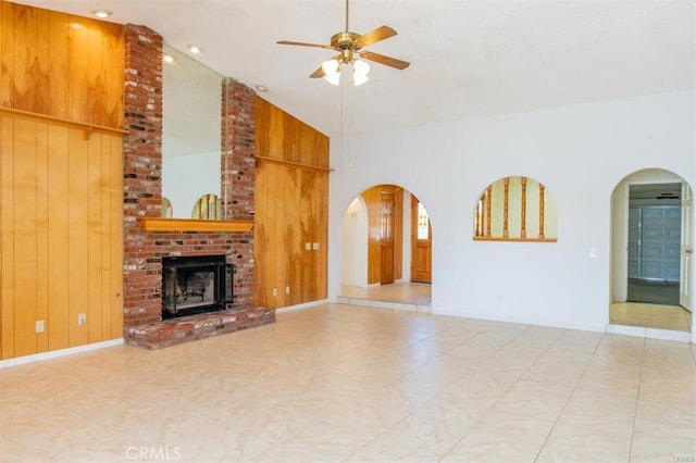 unfurnished living room featuring wooden walls, a brick fireplace, ceiling fan, arched walkways, and high vaulted ceiling