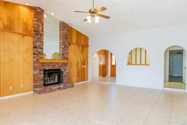 unfurnished living room featuring high vaulted ceiling, arched walkways, wooden walls, ceiling fan, and a fireplace