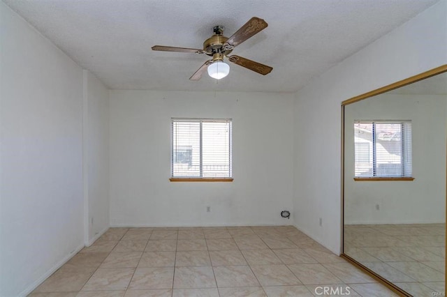 empty room with light tile patterned flooring, a textured ceiling, ceiling fan, and plenty of natural light