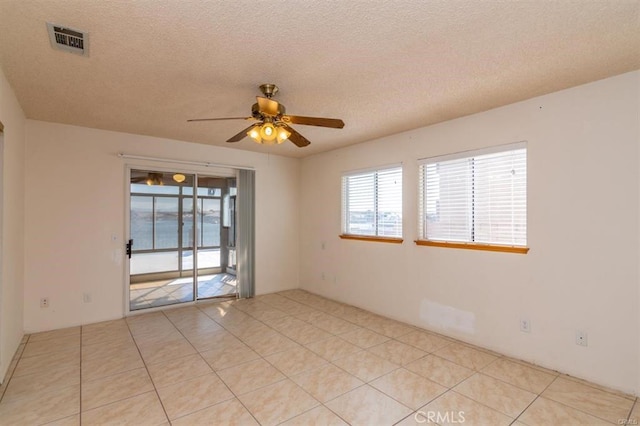 empty room featuring light tile patterned floors, a ceiling fan, visible vents, and a textured ceiling