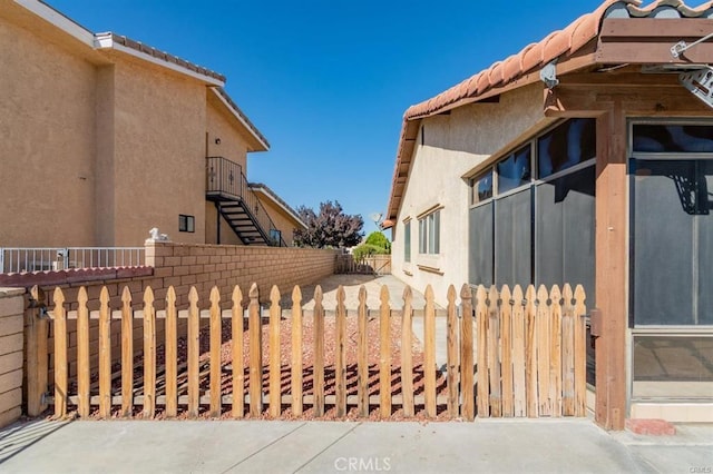 view of property exterior with stairs, a tiled roof, fence private yard, and stucco siding