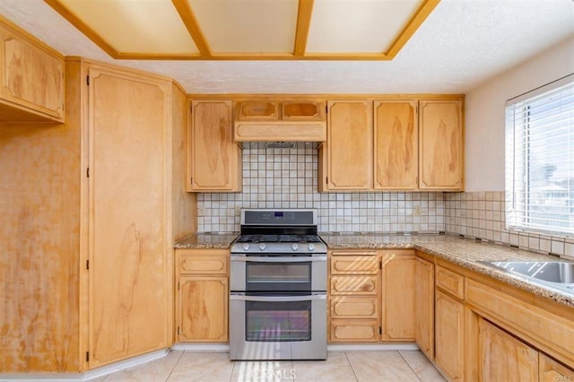 kitchen featuring premium range hood, range with two ovens, decorative backsplash, light tile patterned flooring, and a sink