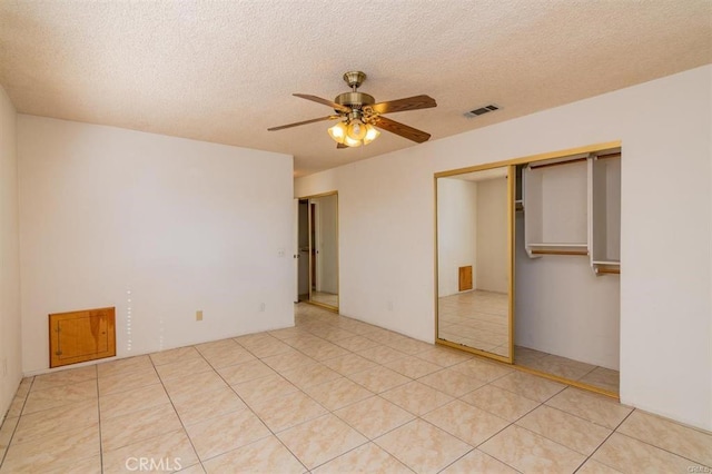 unfurnished bedroom with a closet, light tile patterned flooring, a textured ceiling, visible vents, and ceiling fan
