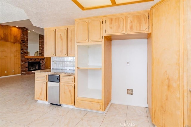 kitchen with light tile patterned floors, a fireplace, light brown cabinetry, wood walls, and a textured ceiling