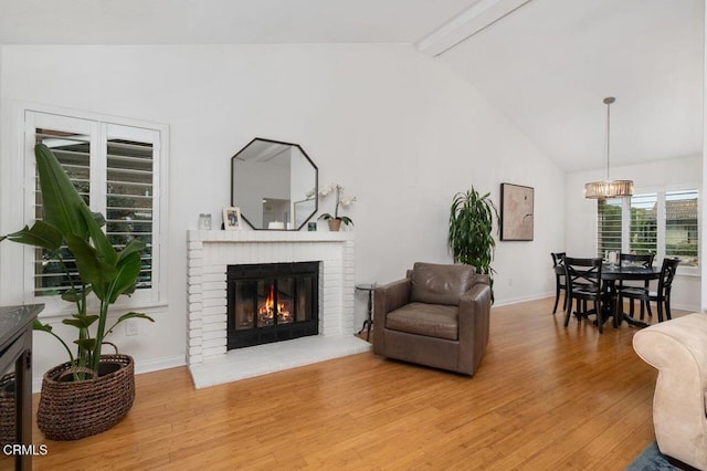 living area with beam ceiling, light wood finished floors, an inviting chandelier, a brick fireplace, and baseboards