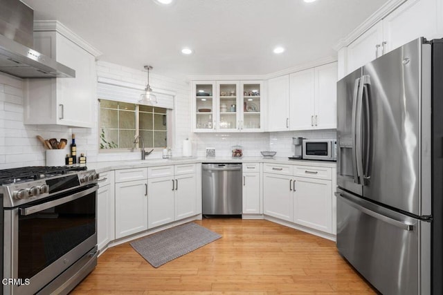 kitchen featuring wall chimney exhaust hood, stainless steel appliances, light wood-type flooring, white cabinetry, and a sink